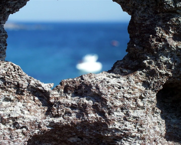 a white boat in the distance out from a cave near a cliff