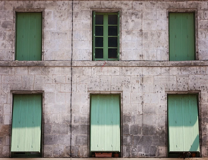 several windows and green shutters on a gray wall