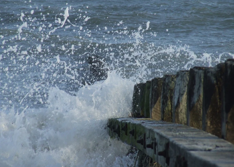 a rock jetty in the water is in front of a crashing wave