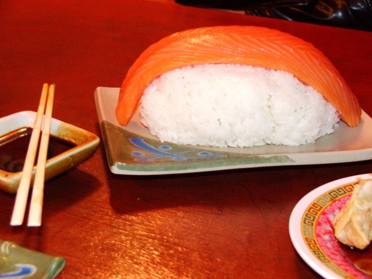 a wooden table topped with a plate of rice covered sushi