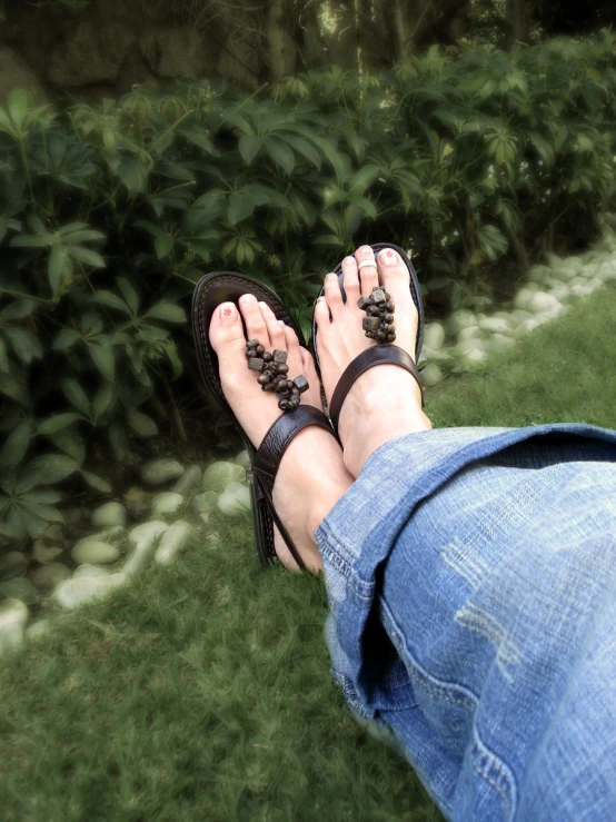 a woman's bare feet wearing sandals standing in a grassy field