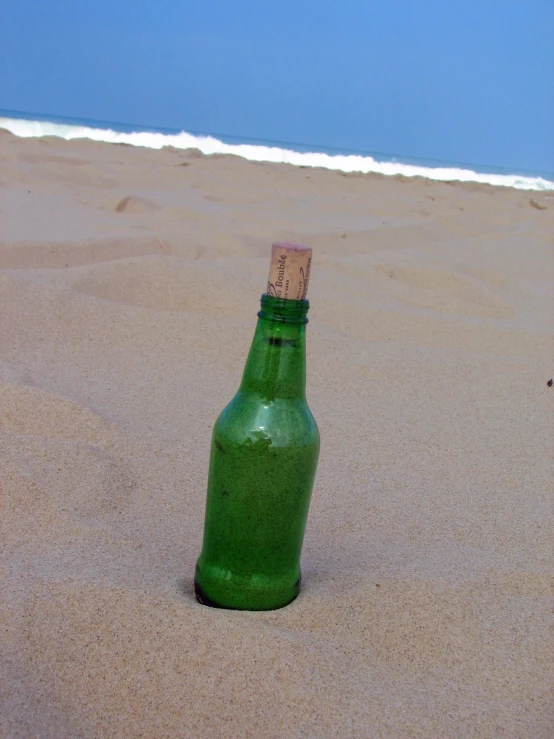 the green bottle is placed on the sand near water