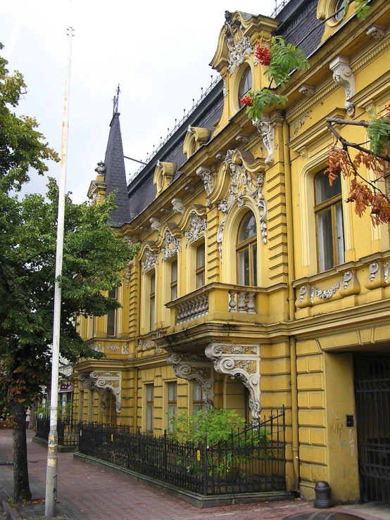 old yellow building on street corner with large trees and fence