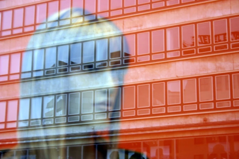 person with clock on red building reflected in window