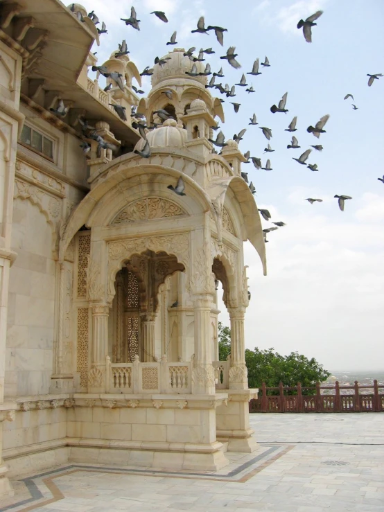 birds fly in the sky above a stone building