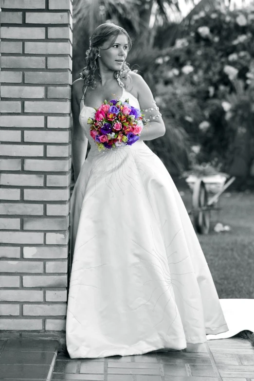 a bride poses outside by a brick wall in the sun