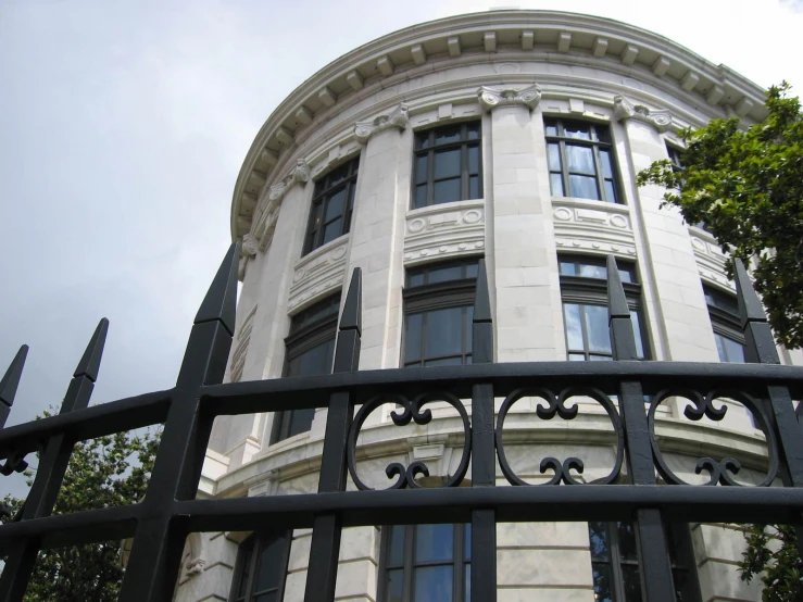 an ornate building seen through a fence with trees in the background