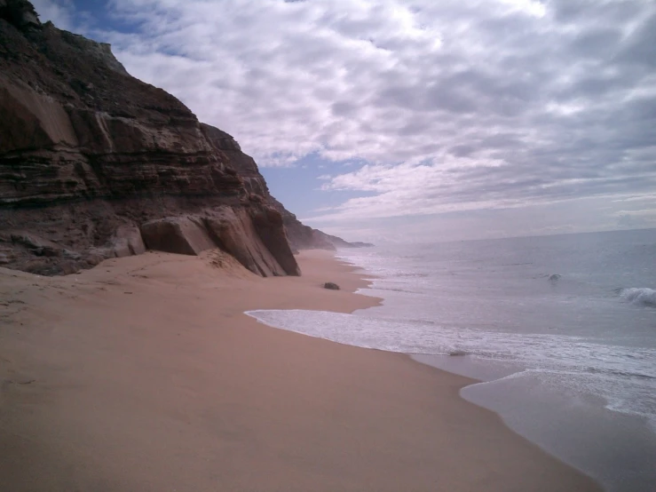 a sandy beach next to a large cliff