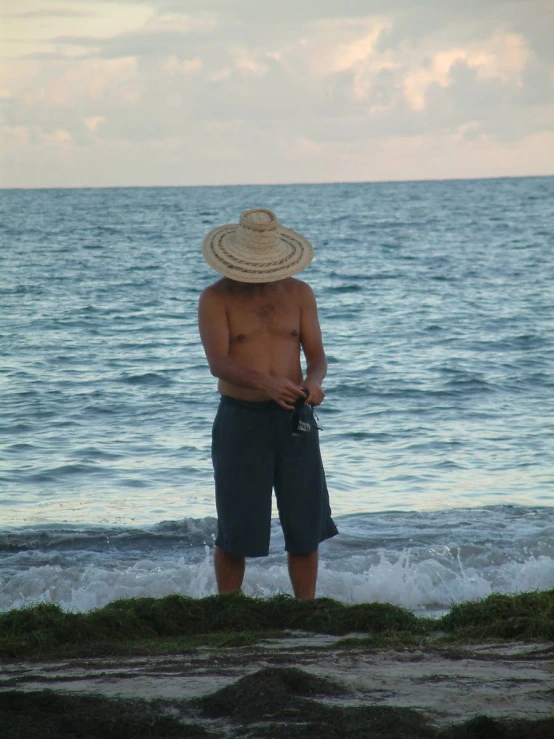 a man standing at the beach wearing a hat