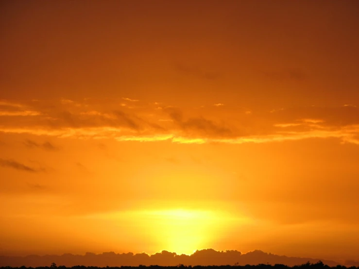 the sun setting in an orange sky above a small boat