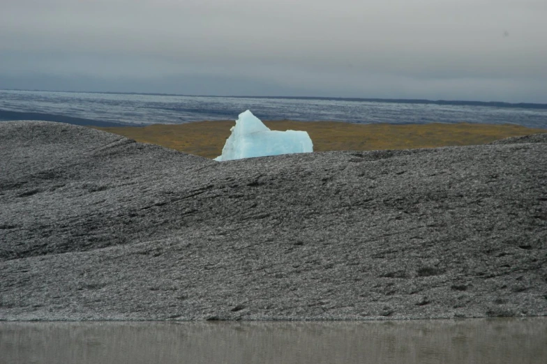 an iceberg sitting on top of a rocky hill next to the ocean