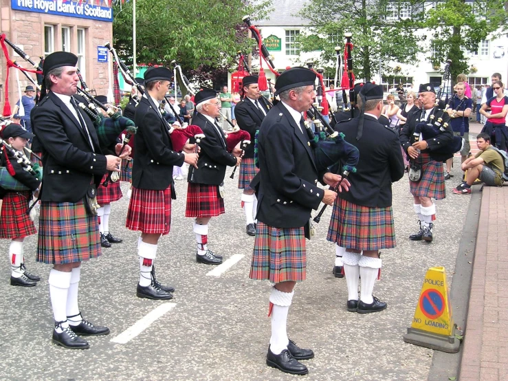 some men are dressed in tartan kilts and playing instruments