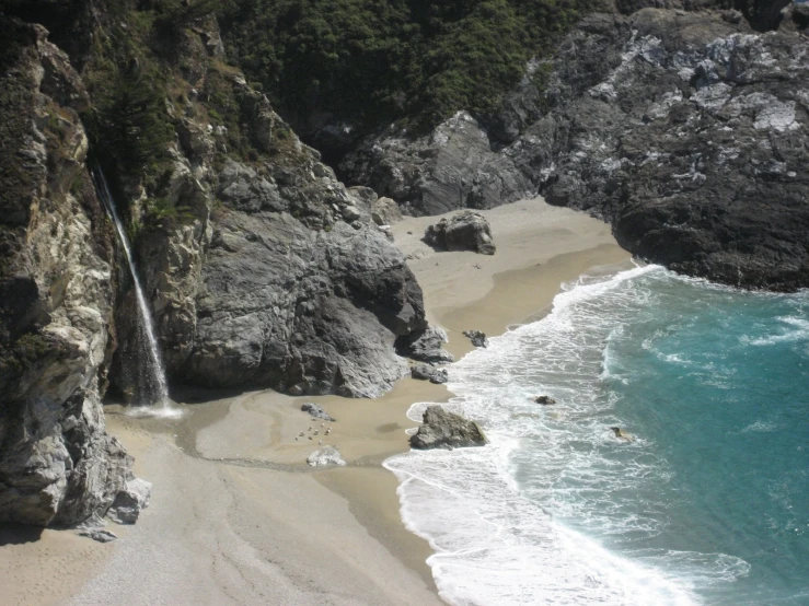 a small waterfall next to the ocean next to the cliffs