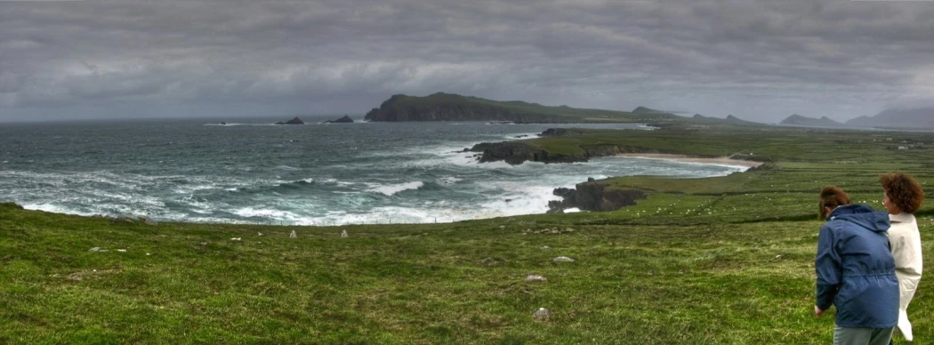 two people standing in front of the ocean under a gray cloudy sky