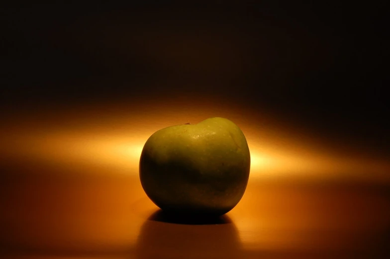 a single green apple sitting in front of a lit back room