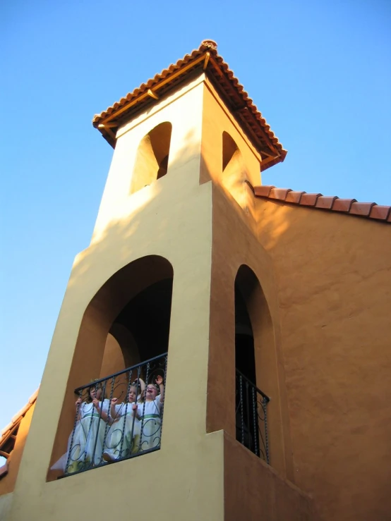 several people in dresses are standing on a balcony near a building