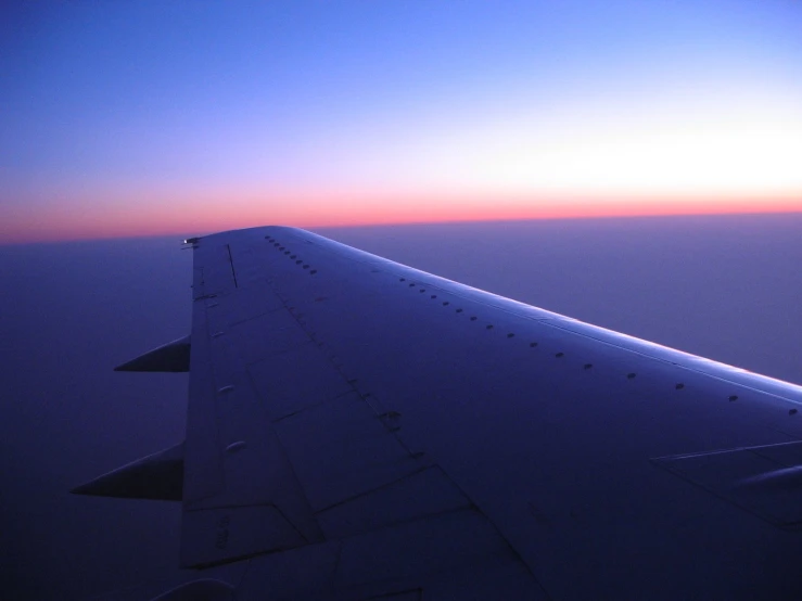an airplane wing flying high into the sky at sunset