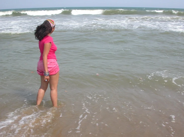 a little girl standing in the ocean next to the beach