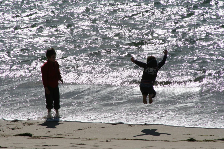 two people jump into the surf with their hands in the air