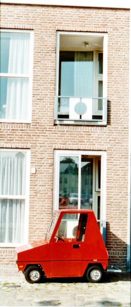 a small red car parked in front of a brick building