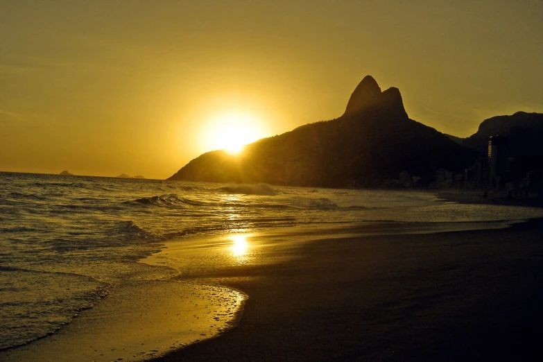 the sun rises over the ocean as it casts the silhouettes of three mountains