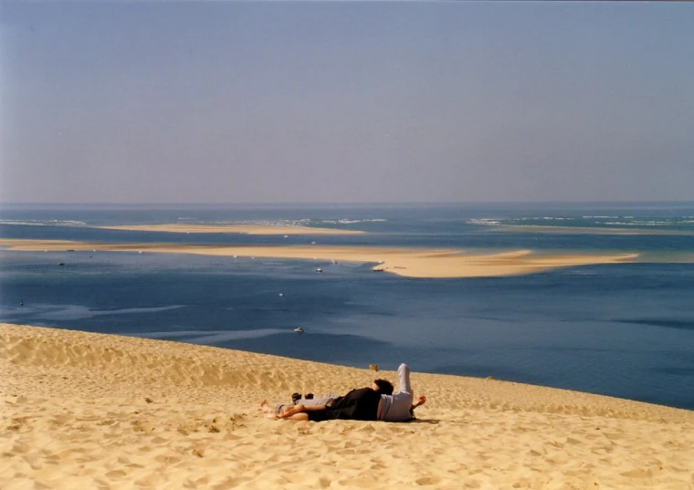 a man is laying down on the sand by the water