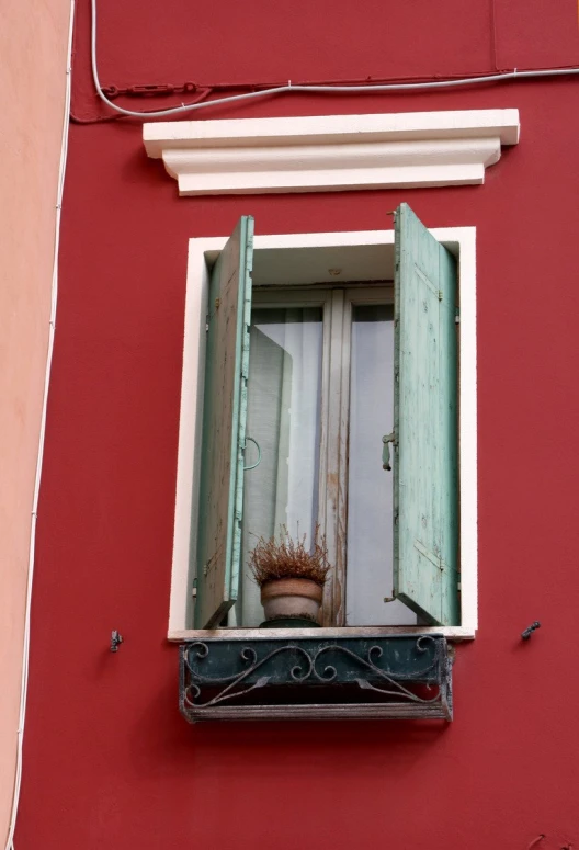 a red building has green shutters and a potted plant in the window