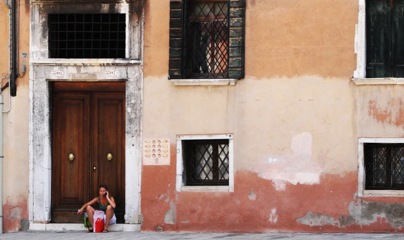 a woman sitting on the steps of a door way in front of a building