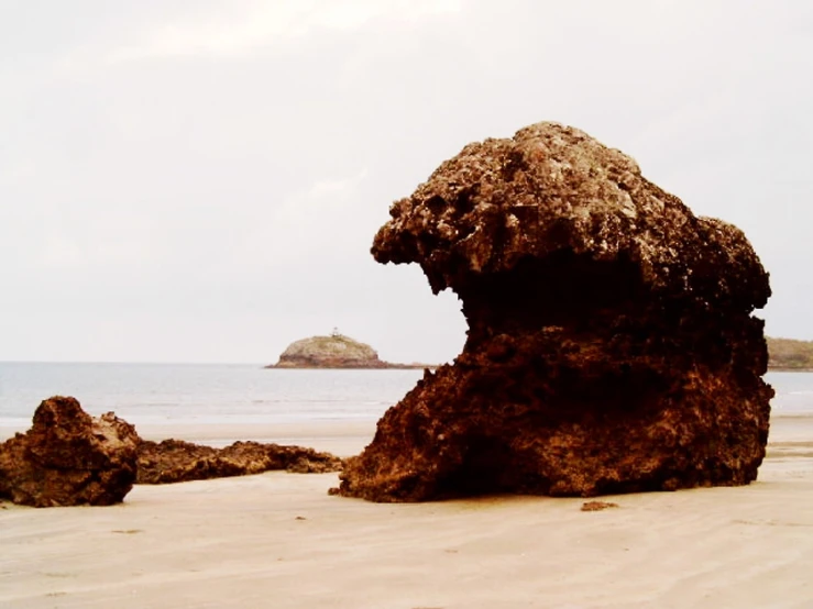 a very big rock by some water by the beach