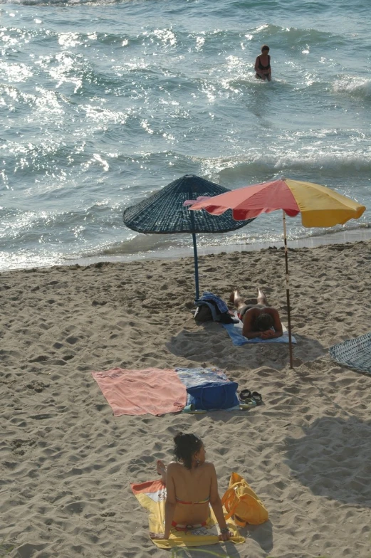 a beach scene with people sitting in the sand and an umbrella and towels on the beach