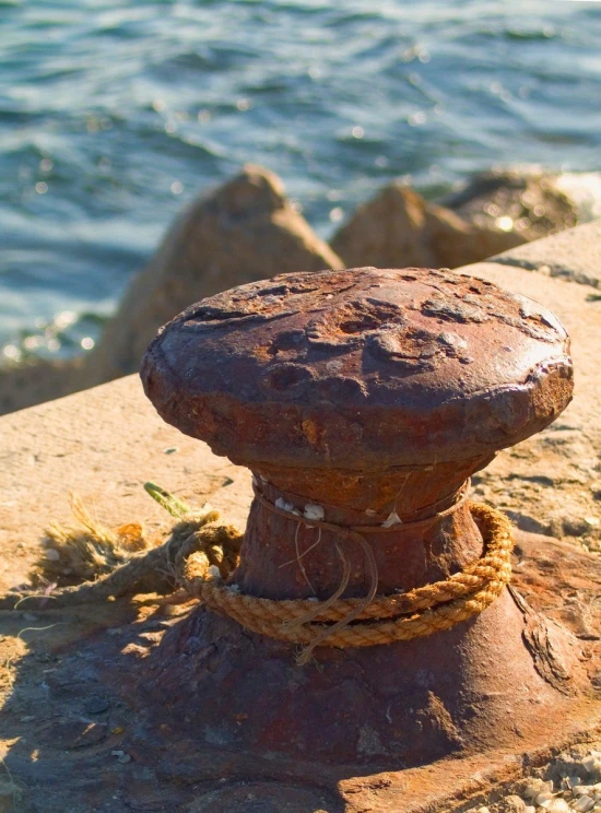 a rusty old iron pole that is tied up to a rock next to the ocean