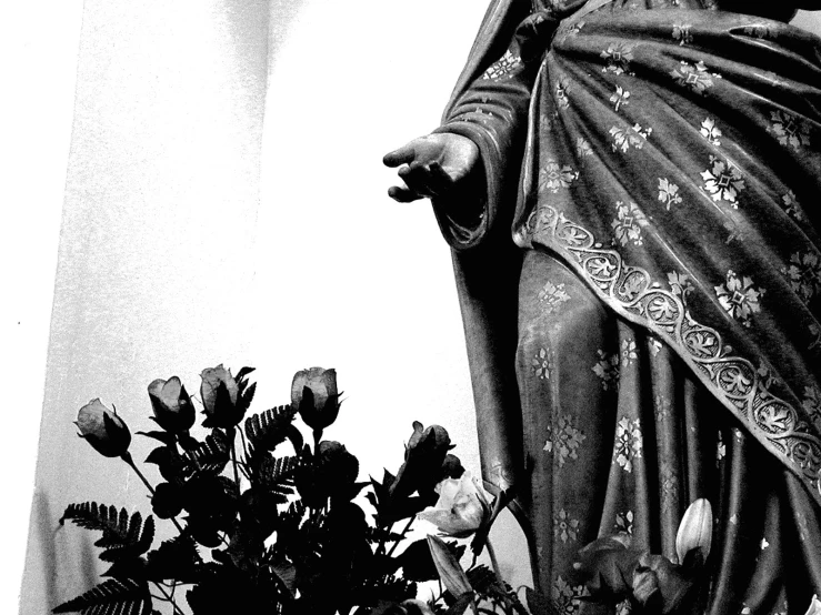 a black and white image of a statue with flowers next to it