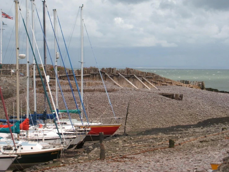 three sailboats sitting at the shore near a rocky beach