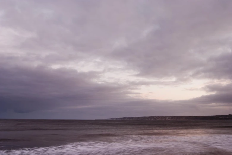 an overcast day on the beach with a person standing in the water