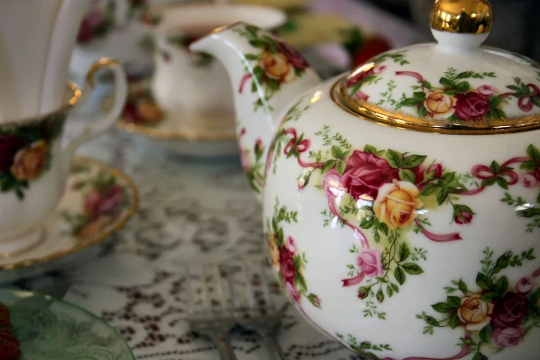 a tea pot with roses sits on a table next to plates