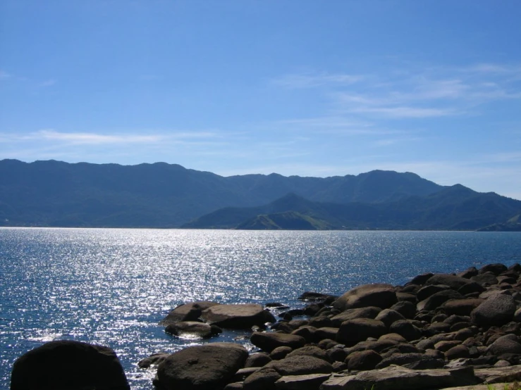 a body of water with rocky shore line and mountains in the distance