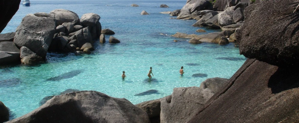 some rocks and blue water and one has a man swimming
