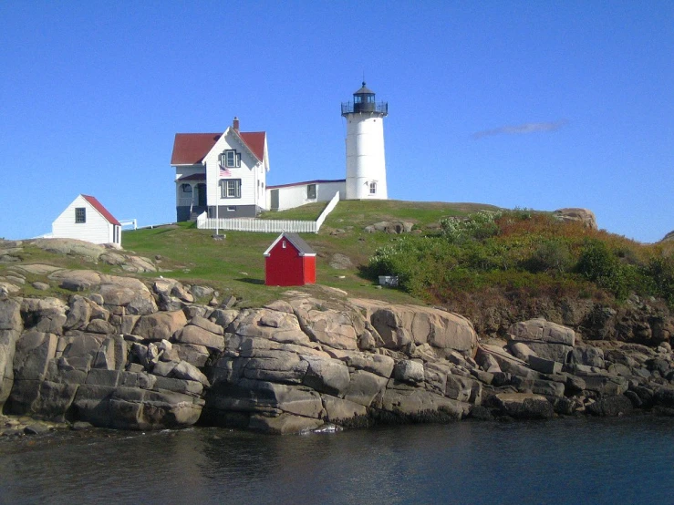 a red and white house with a red door sits atop a rocky shoreline