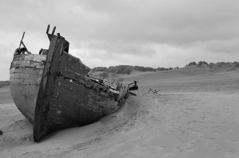 a rusted out boat on sand in a black and white po