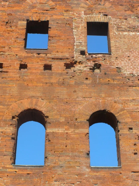 a large brick wall has three windows with sky view