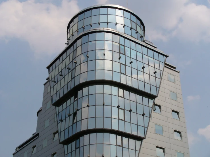 an odd shaped building has many windows and is reflecting the sky