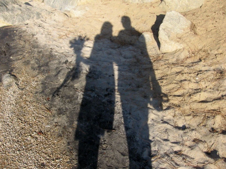 shadow of two people on the sand by rocks