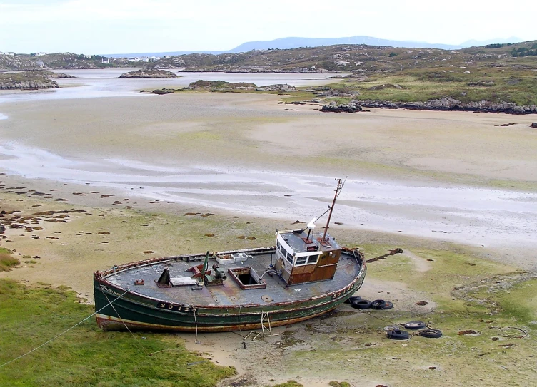 a green boat sitting on top of a sandy shore