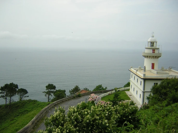 the lighthouse overlooks the ocean from a hill above a building
