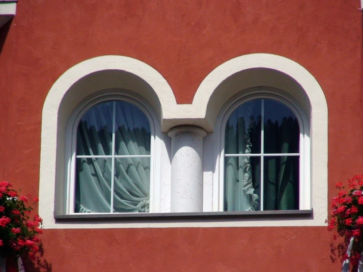 a red wall and two white arched windows with red flowers