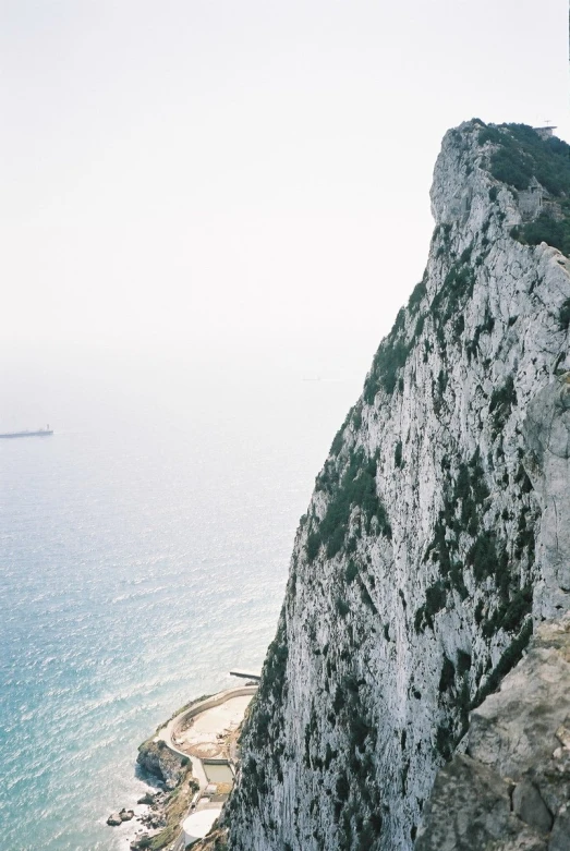 a man standing on a ledge of some cliffs with a boat in the distance