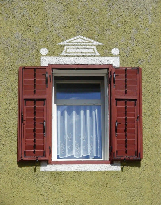 the window with red shutters is closed and has a small curtain drawn on it