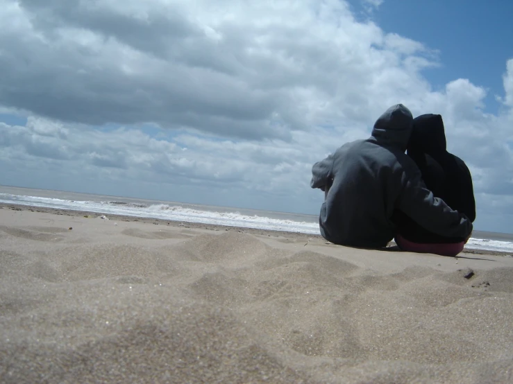 two people sitting on top of sand near the ocean