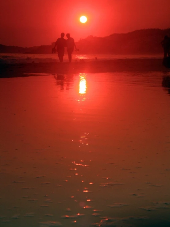 the sun sets over some water with two people