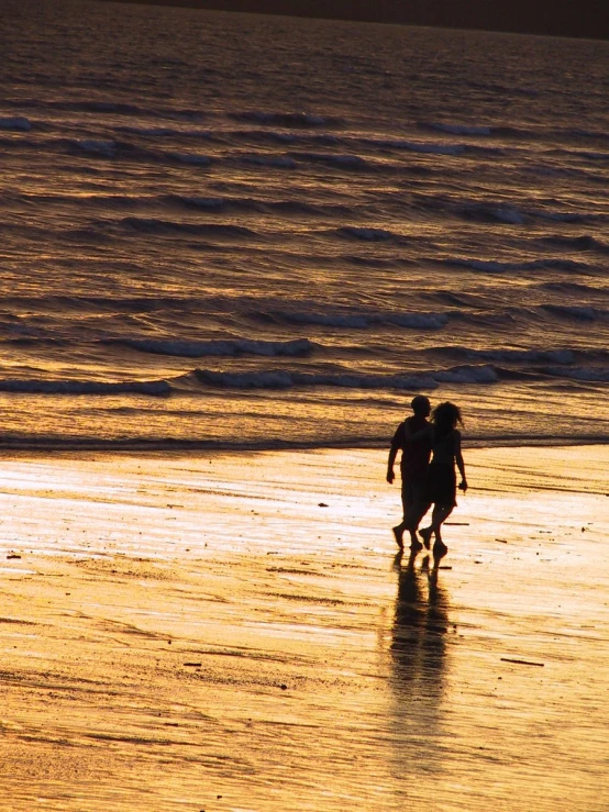 a couple are walking along the beach at sunset